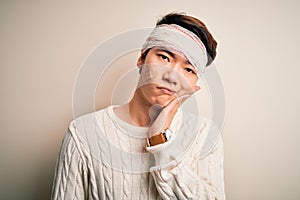 Young handsome chinese man injured for accident wearing bandage and strips on head thinking looking tired and bored with