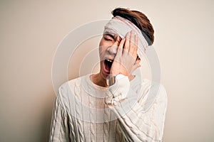 Young handsome chinese man injured for accident wearing bandage and strips on head Yawning tired covering half face, eye and mouth