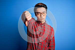 Young handsome chinese man wearing casual shirt and glasses over blue background looking unhappy and angry showing rejection and