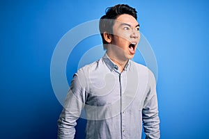 Young handsome chinese man wearing casual shirt standing over isolated blue background angry and mad screaming frustrated and