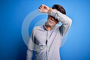 Young handsome chinese man wearing casual shirt standing over isolated blue background covering eyes with arm, looking serious and