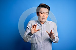 Young handsome chinese man wearing casual shirt standing over isolated blue background disgusted expression, displeased and