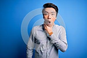 Young handsome chinese man wearing casual shirt standing over isolated blue background Looking fascinated with disbelief, surprise