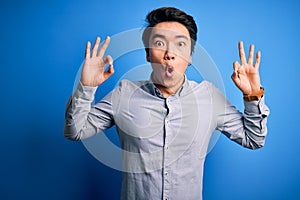 Young handsome chinese man wearing casual shirt standing over isolated blue background looking surprised and shocked doing ok