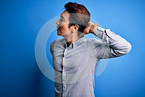 Young handsome chinese man wearing casual shirt standing over isolated blue background Suffering of neck ache injury, touching