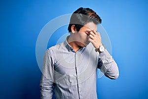 Young handsome chinese man wearing casual shirt standing over isolated blue background tired rubbing nose and eyes feeling fatigue
