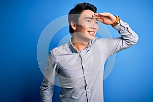 Young handsome chinese man wearing casual shirt standing over isolated blue background very happy and smiling looking far away