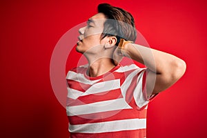 Young handsome chinese man wearing casual striped t-shirt standing over red background Suffering of neck ache injury, touching