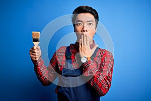 Young handsome chinese painter man wearing apron painting using brush cover mouth with hand shocked with shame for mistake,