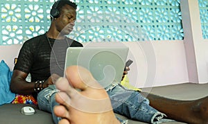 Young handsome and cool black African American hipster man with headphones networking relaxed with mobile phone and laptop