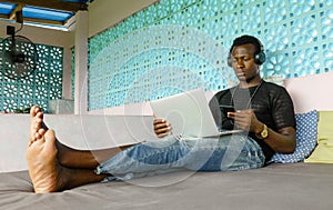 Young handsome and cool black African American hipster man with headphones networking relaxed with mobile phone and laptop