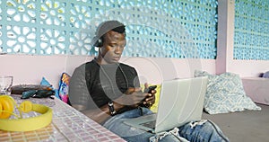 Young handsome and cool black African American hipster man with headphones networking relaxed with mobile phone and laptop