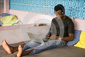 Young handsome and cool black African American hipster man with headphones networking relaxed with mobile phone and laptop