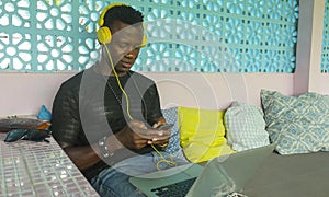 Young handsome and cool black African American hipster man with headphones networking relaxed with mobile phone and laptop