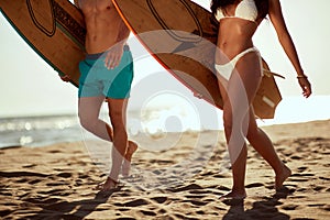 Young handsome couple of surfers is holding surfboards and enjoying a walk the beach at sea. Summer, vacation, sea, together