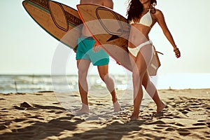Young handsome couple of surfers with surfboards is enjoying warm sand while walking the beach at sea. Summer, vacation, sea,