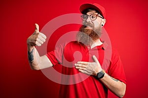 Young handsome delivery man wearing glasses and red cap over isolated background Looking proud, smiling doing thumbs up gesture to