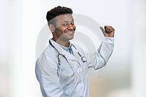 Young handsome doctor with stethoscope pointing aside with finger.