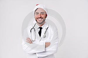 Young handsome doctor in white uniforme and Santa Claus hat standing in studio on white background loking at camera abd teeth photo