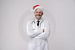 Young handsome doctor in white uniforme and Santa Claus hat standing in studio on white background loking at camera abd teeth photo