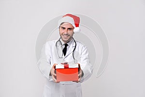 Young handsome doctor in white uniforme and Santa Claus hat standing in studio on white background smile and finger in camera photo