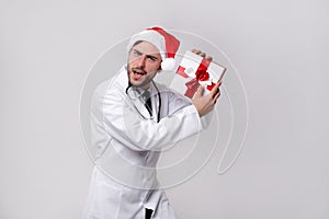 Young handsome doctor in white uniforme and Santa Claus hat standing in studio on white background smile and finger in camera photo