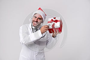 Young handsome doctor in white uniforme and Santa Claus hat standing in studio on white background smile and finger in camera photo