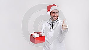 Young handsome doctor in white uniforme and Santa Claus hat standing in studio on white background smile and finger in camera photo