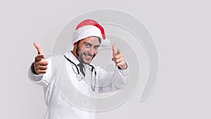 Young handsome doctor in white uniforme and Santa Claus hat standing in studio on white background smile and finger in camera photo