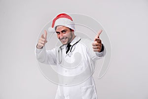 Young handsome doctor in white uniforme and Santa Claus hat standing in studio on white background smile and finger in camera photo