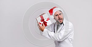 Young handsome doctor in white uniforme and Santa Claus hat standing in studio on white background smile and finger in camera photo