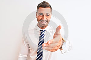 Young handsome elegant business man over isolated background smiling friendly offering handshake as greeting and welcoming