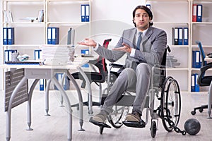The young handsome employee in wheelchair working in the office