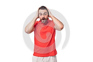 young handsome european brunette man with a beard dressed in a red t-shirt looks at the camera in surprise