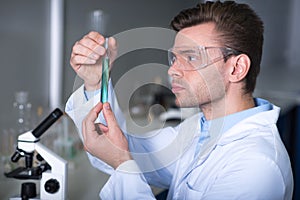 Young handsome explorer keeping and overlooking test tube.