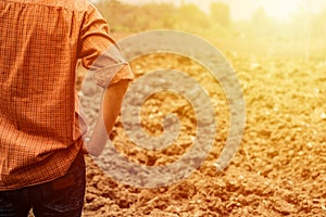 A young handsome farmer looking at his farm. An empty land. Farmer standing in a wheat field with hands on hips and looking