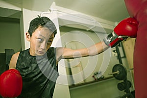 Young handsome and fierce teenager boy doing fight workout punching heavy bag looking cool and badass at fitness club training