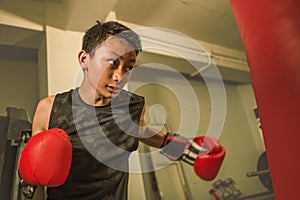 Young handsome and fierce teenager boy doing fight workout punching heavy bag looking cool and badass at fitness club training