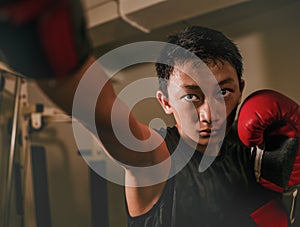 Young handsome and fierce teenager boy doing fight workout punching heavy bag looking cool and badass at fitness club training