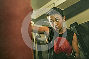 Young handsome and fierce teenager boy doing fight workout punching heavy bag looking cool and badass at fitness club training