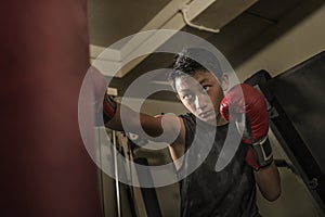 Young handsome and fierce teenager boy doing fight workout punching heavy bag looking cool and badass at fitness club training