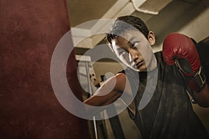 Young handsome and fierce teenager boy doing fight workout punching heavy bag looking cool and badass at fitness club training