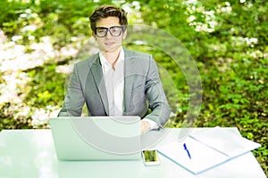 Young handsome freelance working at laptop at office table in green park. Business concept.
