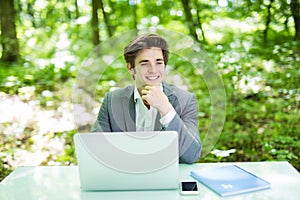 Young handsome freelancer working at laptop at office table in green park. Business concept.