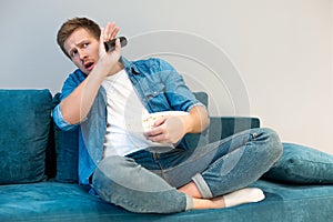 Young handsome frightened man watching scary movie on the sofa eating popcorn feeling comfortable at home