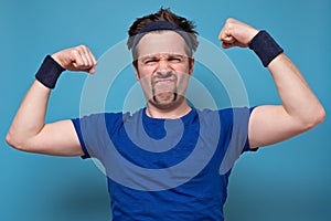 Young handsome funny man wearing holding his arm up to show how strong he is