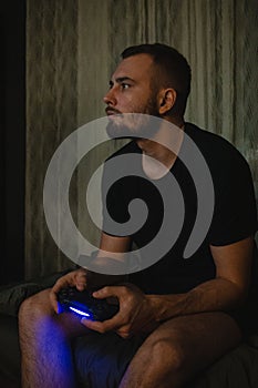 Young handsome gamer man with beard in black t-shirt playing video game using joystick with a concetration on smart face thinking