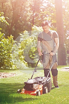 Handsome gardener waring brown overall and mowing the grass photo