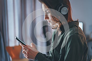 Young handsome girl relaxing at modern home,wearing casual clothes,playing music on smartphone and listening audio books