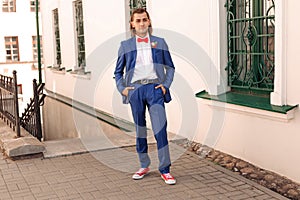 Young handsome groom in red sneakers stand in a city street background.